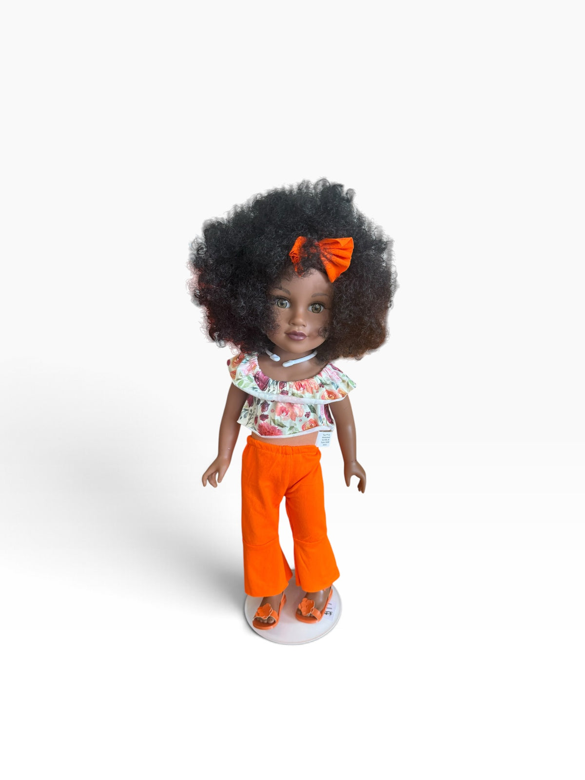 Our Generation doll with dark curly hair, orange bow, floral top, and orange pants and shoes